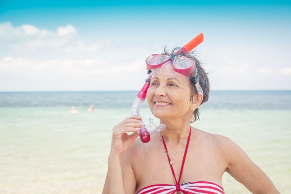 Mature woman in snorkel gear standing on the beach smiling