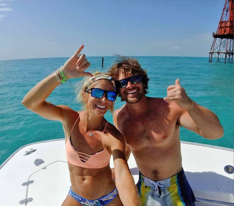 Photo of Jennifer and Matt Parramore sitting on the back of their boat. They are in swimsuits ands are looking at the camera with their thumbs up and smiling.
